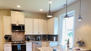 A modern kitchen with white cabinets, a granite countertop, stainless steel appliances, and a bar area with stools. - Historic Schoolhouse on Winery Row (Purcellville)