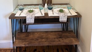 A dining table with a glass top, set with white plates, silverware, and blue glassware. Above the table is a framed painting of a cow. - Historic Schoolhouse on Winery Row (Purcellville)