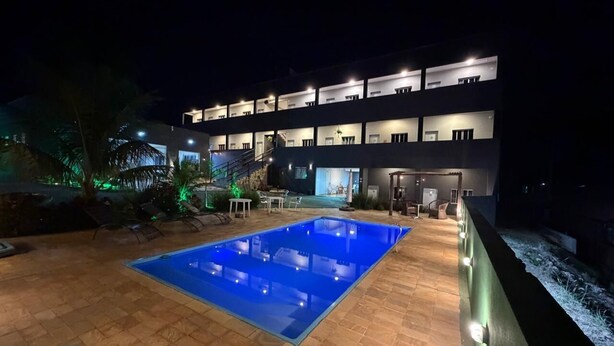 Una piscina con solárium empedrado, un edificio de varios pisos con ventanas iluminadas y una escalera que lleva a los pisos superiores.