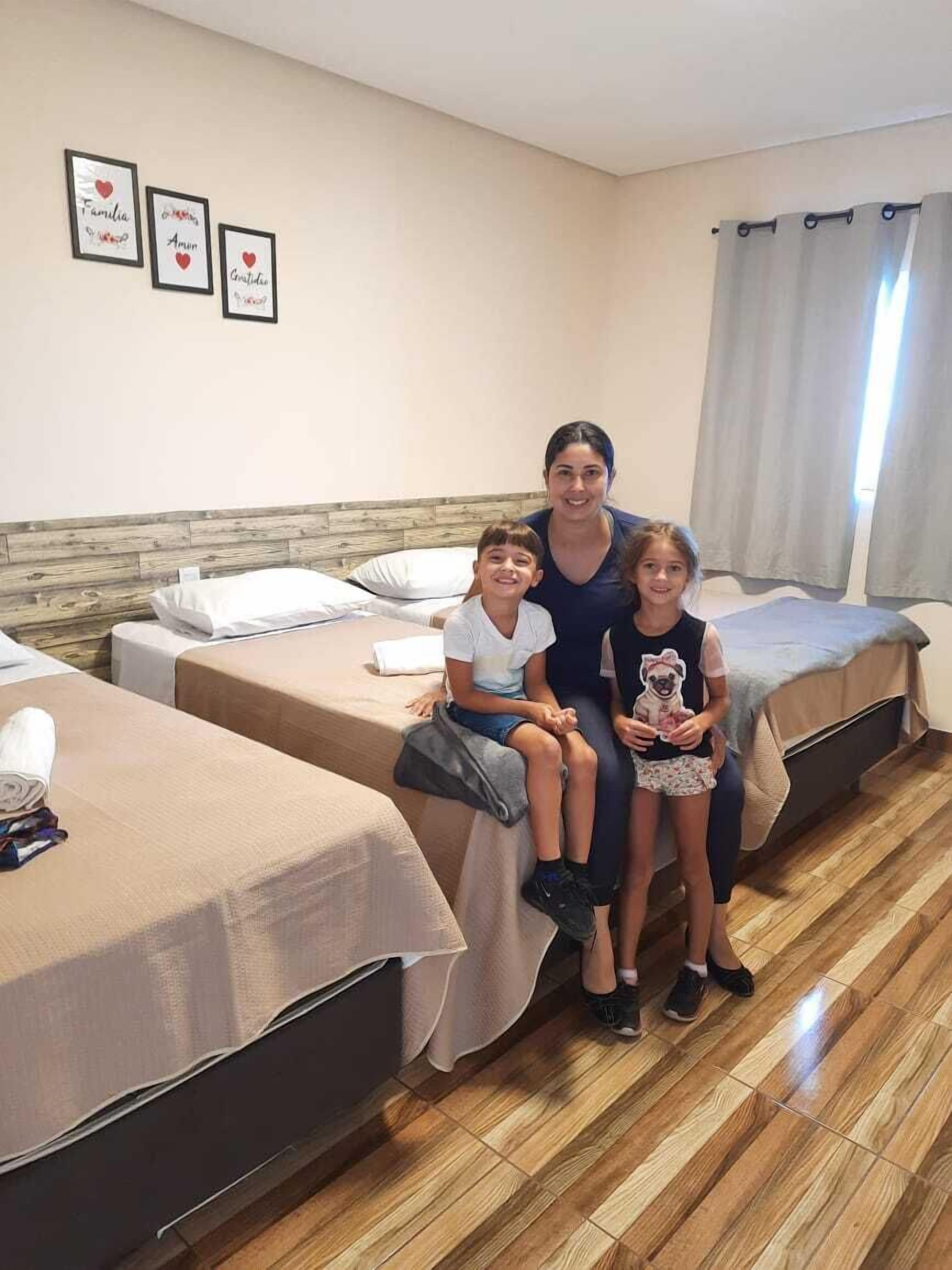 Habitación de hotel con dos camas individuales, cabecera de madera, ventana con cortinas y tres cuadros enmarcados en la pared.