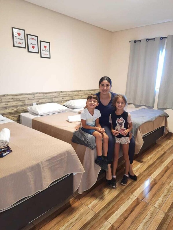 Une chambre d’hôtel avec deux lits simples, une tête de lit en bois, une fenêtre avec des rideaux et trois tableaux encadrés accrochés au mur.