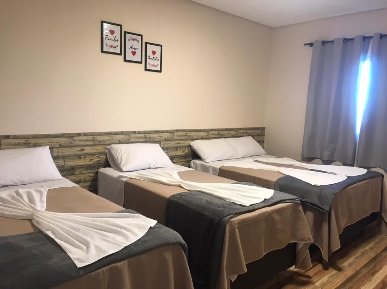 A room with three beds, each with a wooden headboard and white bedding. There are framed pictures on the wall above the beds.