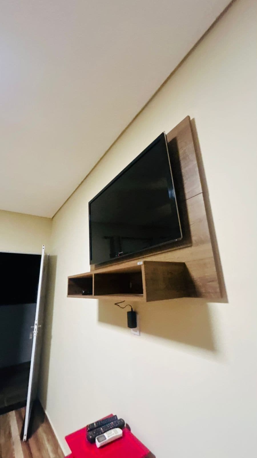 A television mounted on a wall with a wooden shelf below it.