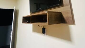 A television mounted on a wall with a wooden shelf below it.