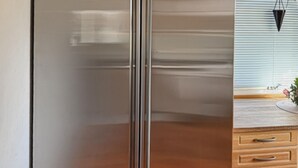 A modern kitchen with a stainless steel refrigerator, wooden cabinets, and a window with blinds. - Pet friendly home in Lidköping (Lidköping)