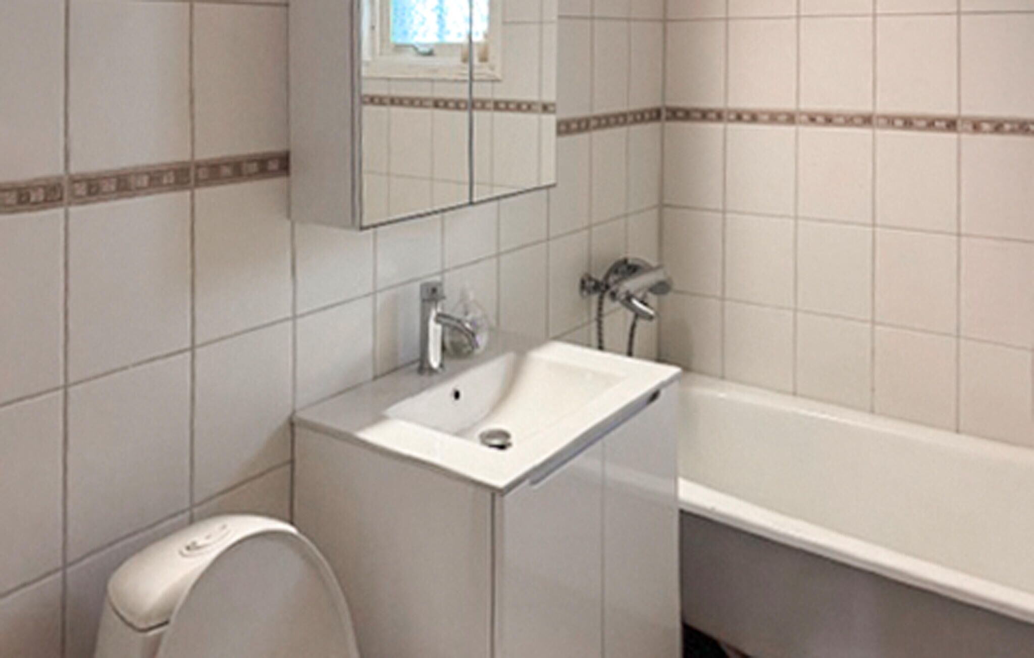 Un baño con lavamanos blanco, espejo, inodoro y bañera.