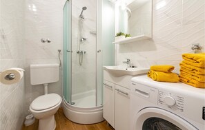 Une petite salle de bain comprenant des toilettes, une douche, un lavabo et un lave-linge.