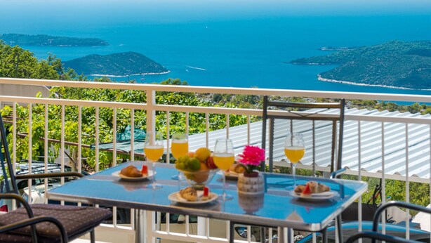 Een balkon met een ontbijttafel, met uitzicht op een schilderachtige kustlijn met eilanden en helderblauw water.