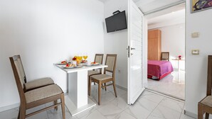 Hotelkamer met een zithoek, met een tafel gedekt voor twee personen, twee stoelen en een flatscreen televisie aan de muur.