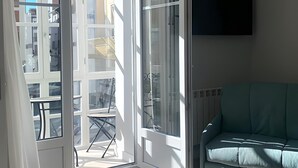 Een kamer met een schuifdeur naar een balkon, een groene bank en een wandgemonteerde flatscreen-televisie.