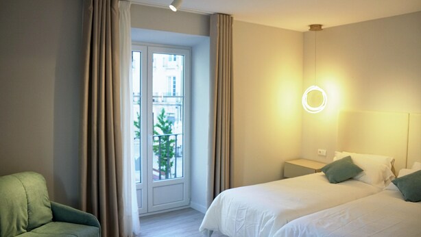 Een hotelkamer met een bed, een stoel, een nachtkastje en een raam met gordijnen.