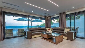 Ein modernes Wohnzimmer mit einer Eckcouch, einem Glastisch und großen Fenstern mit Blick auf den Ozean.