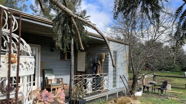Een rustieke hut met een veranda, een houten stoel en een bloempot.