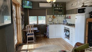 Een kleine keuken met een eethoek, houten vloeren en een aan de muur bevestigde televisie.