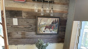 Een rustieke houten eettafel met een vaas groen, een lijst met schilderij en een raam met uitzicht.