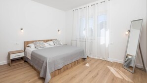 Ein Schlafzimmer mit einem hölzernen Bett, weißer Bettwäsche, einem Nachttisch, einem Spiegel und durchsichtigen Vorhängen.