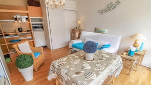 Ein modernes, helles Zimmer mit einem Esstisch, einer Couch, einem Sessel, einer kleinen Pflanze und einer Wanddekoration.