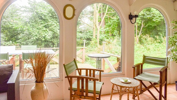 A covered patio with a table and chairs, large arched windows, and a view of greenery. - 2 bedroom gorgeous home in Ystad (Ystad)