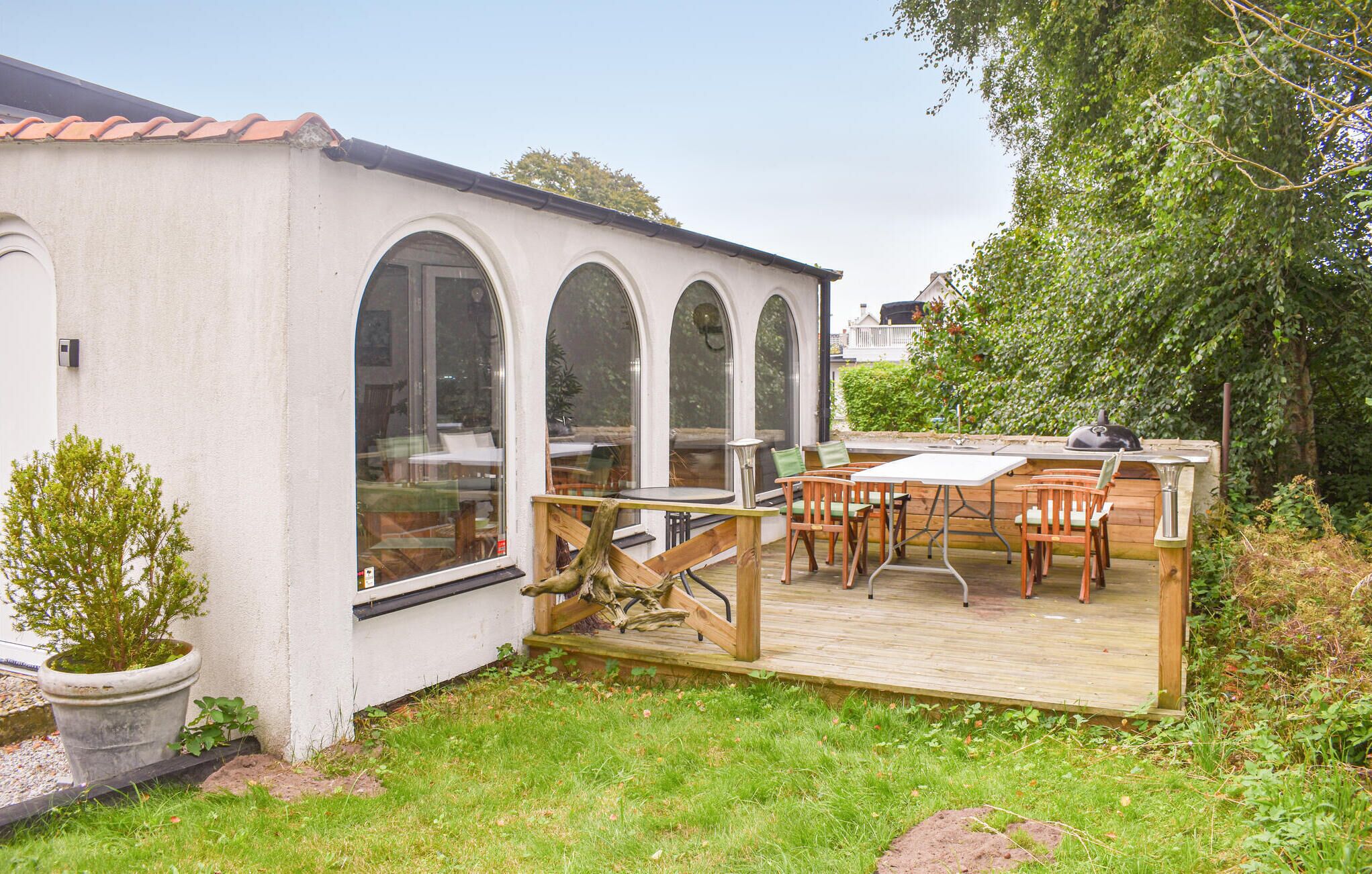 A white building with arched windows and a wooden deck with outdoor seating.