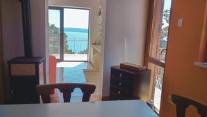 Une pièce avec vue sur la mer, une table, des chaises, un meuble et une petite étagère avec quelques objets.