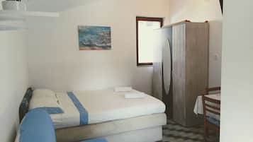 A small, compact room with a bed, a desk, and a chair. There is a painting on the wall and a window with curtains.