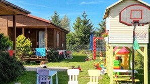 A wooden cabin with a porch, a small basketball court, and a play area with colorful equipment. - 2 bedroom beach front home in Wicie (Wicie)