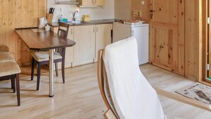 A wooden interior with a dining table, chairs, a kitchen area, and a white chair with a towel. - 2 bedroom beach front home in Wicie (Wicie)