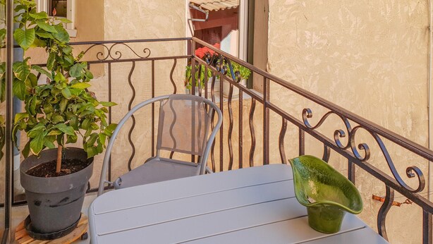 A balcony with a metal railing, a potted plant, a chair, and a table.
