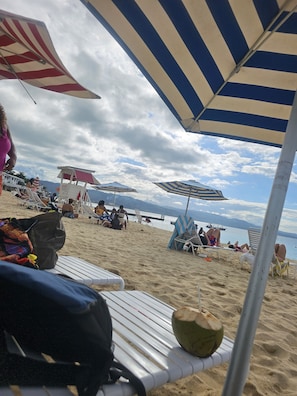 A beach with striped umbrellas, lounge chairs, and a lifeguard tower.