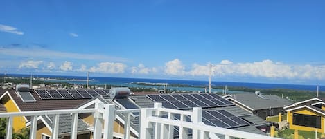 Zona residencial com painéis solares nos telhados, céu azul claro e vista para o oceano.