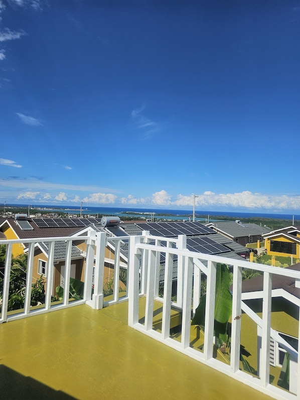 A residential area with solar panels on rooftops, a clear blue sky, and a view of the ocean.