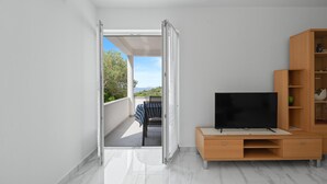 A modern living room with a TV, wooden cabinet, and a balcony with a table and chairs. - Nice apartment in Murter with WiFi (Murter)