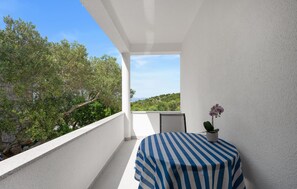 A balcony with a striped table and a potted orchid, overlooking a lush landscape. - Nice apartment in Murter with WiFi (Murter)