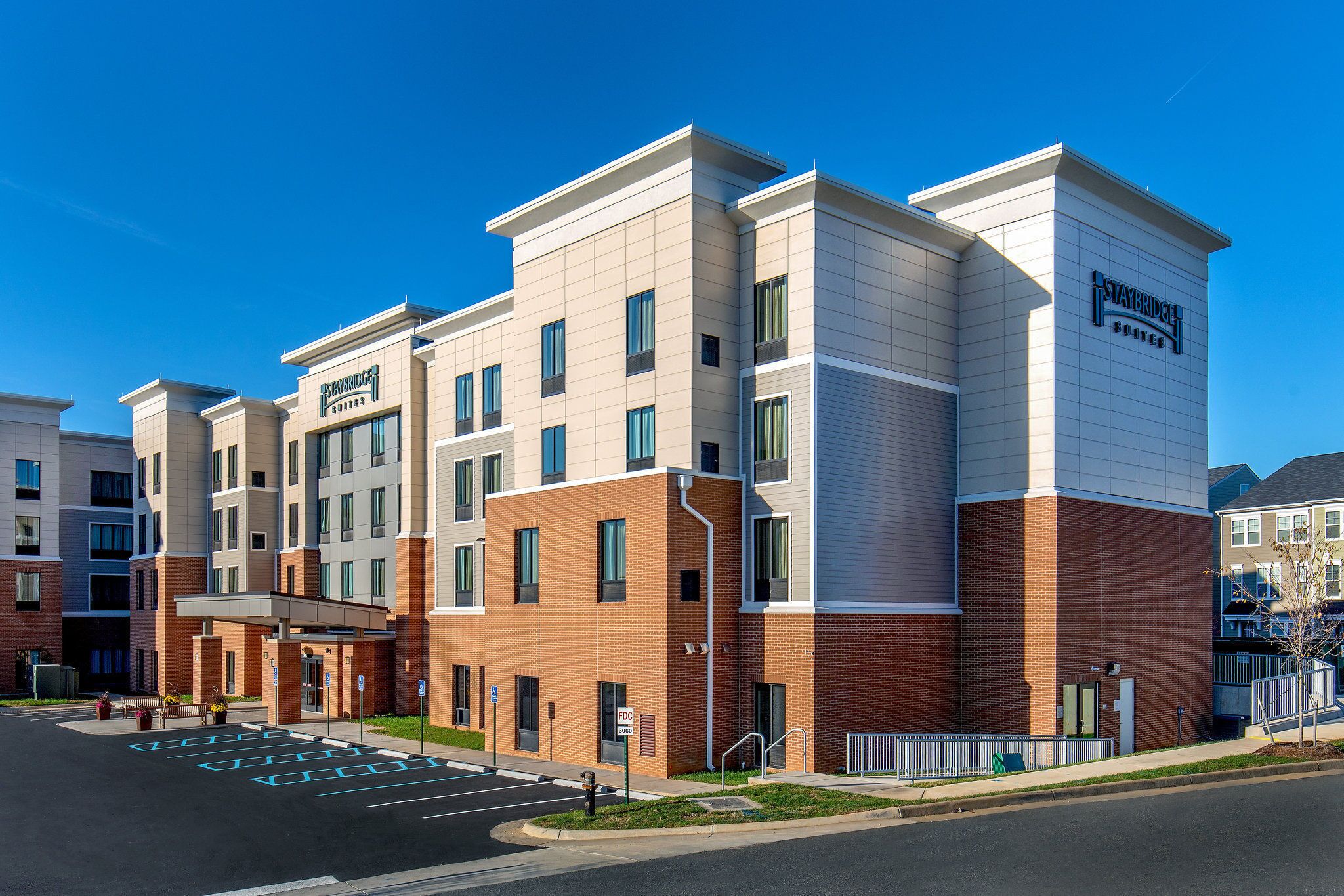 A multi-story hotel with a modern design, featuring a mix of brick and white exterior, a covered entrance, and a clear blue sky.