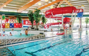 An indoor swimming pool with multiple lanes, a red water slide, and various poolside amenities.