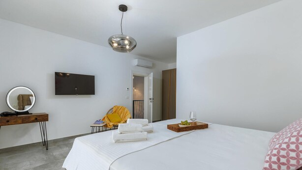 A modern bedroom with a large bed, a bedside table with a mirror, a flat-screen TV, and a small seating area with a chair and a yellow throw blanket. - Nice home in Galizana (Galizana)