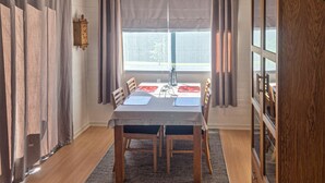 A dining area with a table set for four, a clock on the wall, and a view through a window.