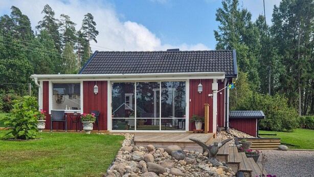 A red house with a tiled roof, large glass doors, and a small porch with chairs.