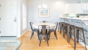 A dining area with a round table and chairs, a kitchen counter with stools, and a framed picture on the wall.