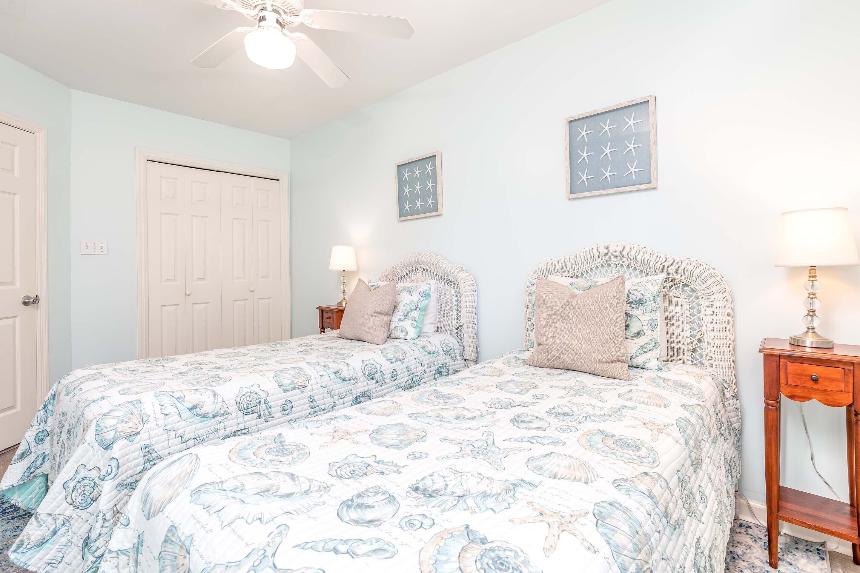 A bedroom with two beds, a ceiling fan, and a nightstand with a lamp.