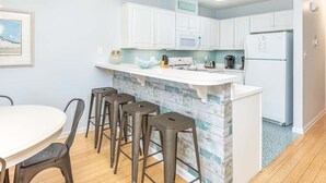 A modern kitchen with white cabinets, a marble island, and bar stools.