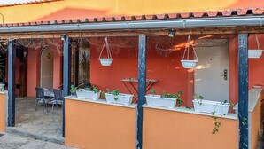 A covered outdoor seating area with tables and chairs, potted plants, and hanging baskets.