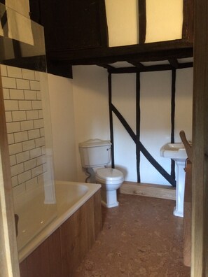 A small bathroom with a toilet, a sink, and a bathtub. The walls are tiled, and there is a wooden floor. - Delightful 4BD Home Full of Flair Edenbridge Kent (Edenbridge)