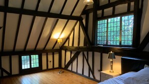 A bedroom with exposed wooden beams, a wooden floor, a bed with white bedding, and two bedside lamps.