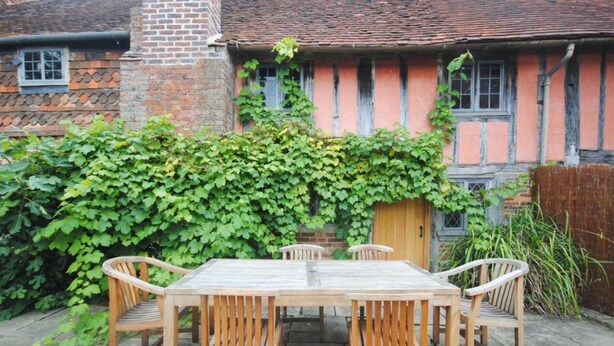 A wooden table and chairs set outdoors with a brick building in the background.