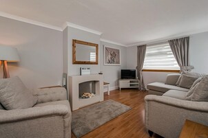 A modern living room with two sofas, a fireplace, a TV, and a large window with curtains.
