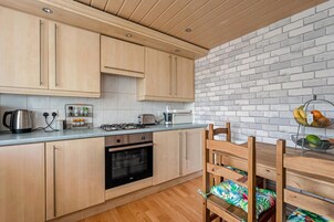 A modern kitchen with wooden cabinets, a gas stove, an oven, and a brick wall.