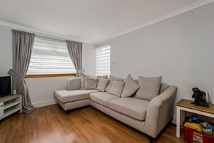 A living room with a beige sectional sofa, a television on a stand, and a small table with a decorative item.