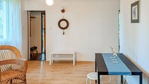 A room with a wooden floor, a wicker chair, a white table with a blue tablecloth, and a small stool.