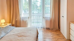A bedroom with a bed, a nightstand, a lamp, a wardrobe, and a window with curtains.